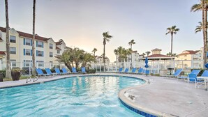 Una piscina con sillas reclinables azules y palmeras.