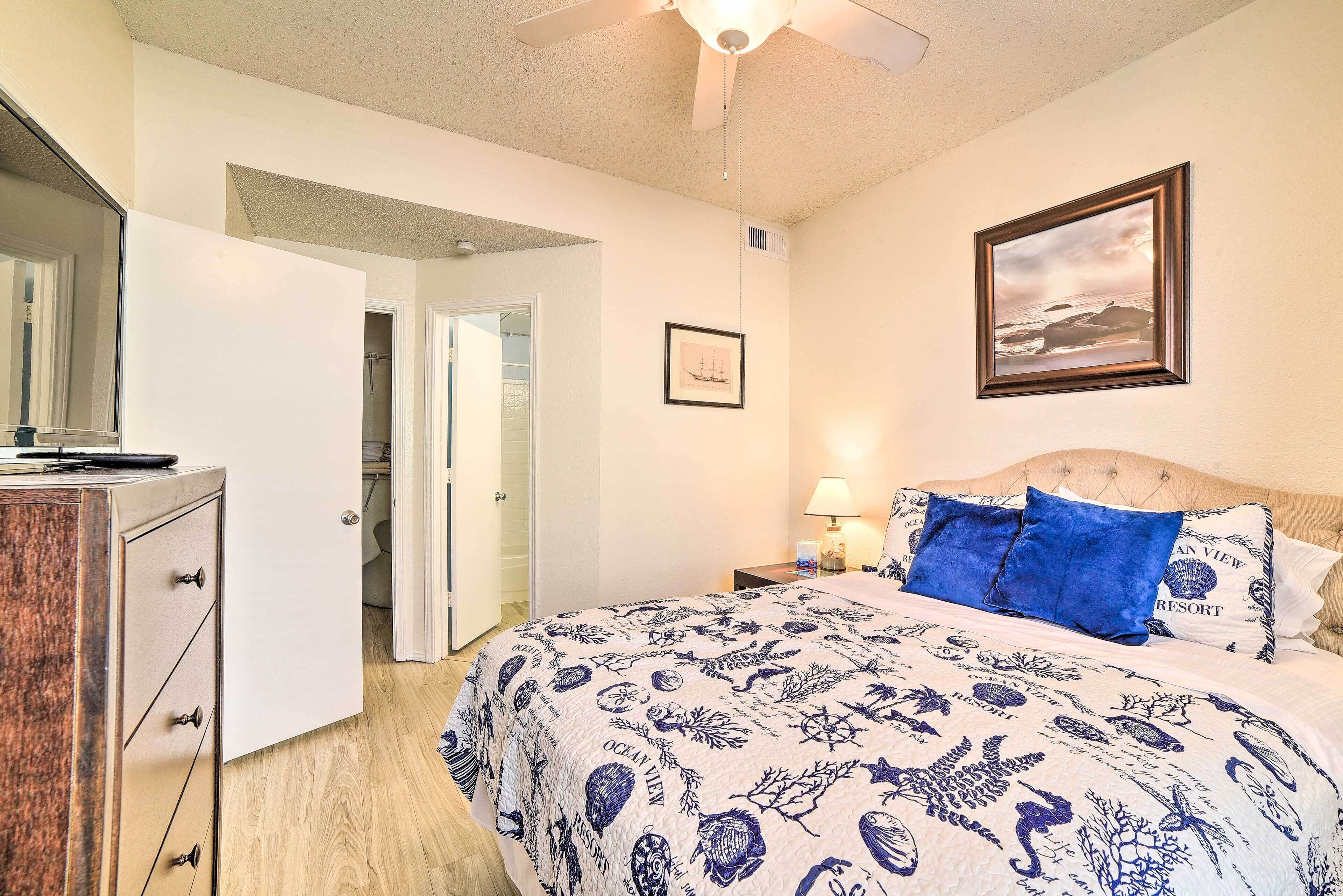 Un dormitorio con una cama, una mesita de noche, una lámpara, un cuadro en la pared y una puerta que da a otra habitación.