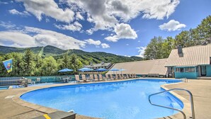 Une piscine entourée d’une clôture et d’arbres, agrémentée de chaises longues et de parasols, avec des montagnes en toile de fond.