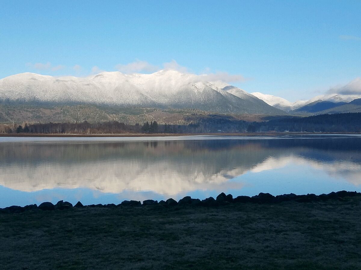 Un lago tranquillo che riflette chiaramente montagne innevate e una riva rocciosa.