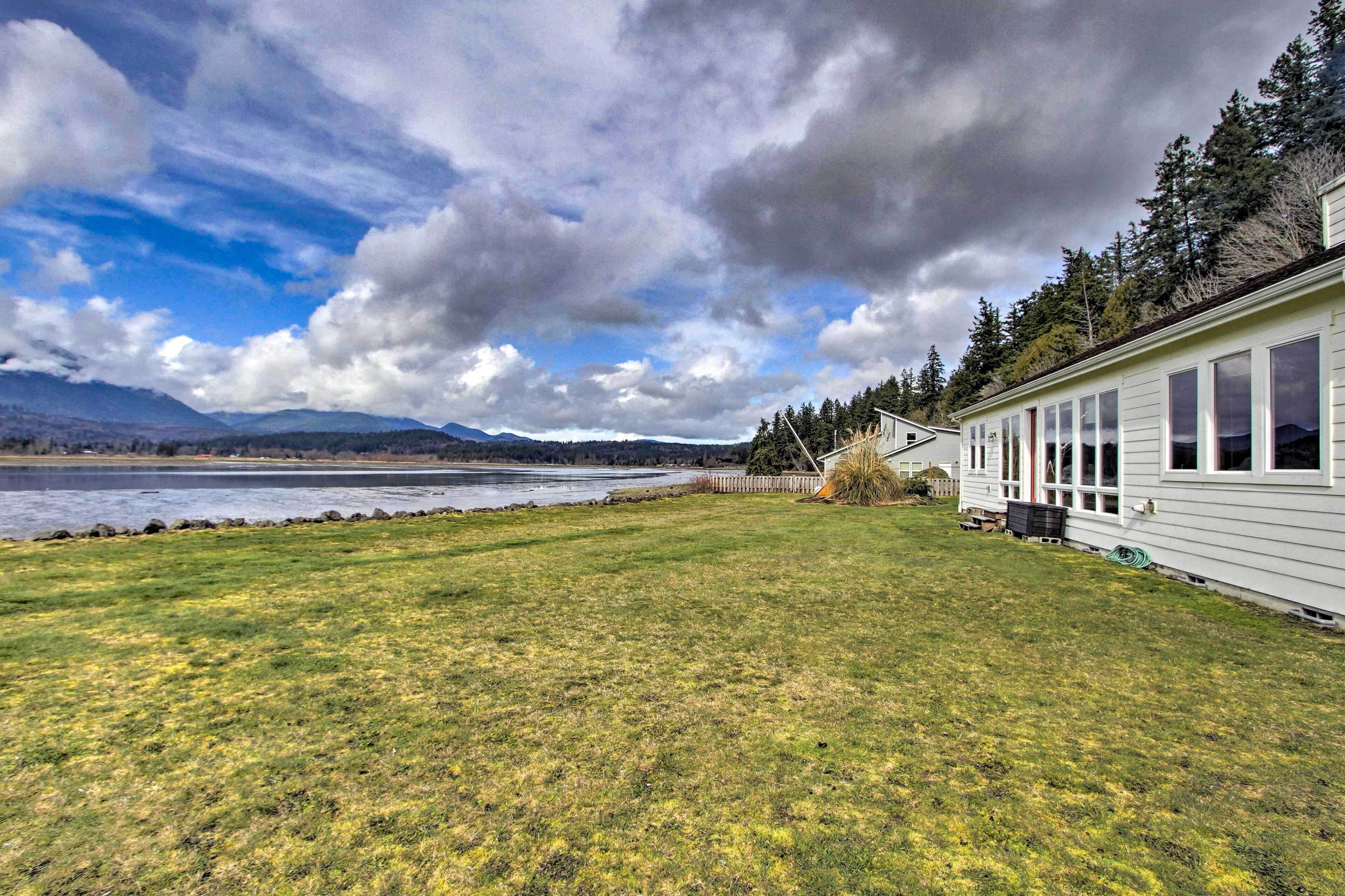 A house with a large lawn, a view of a lake, and mountains in the background.