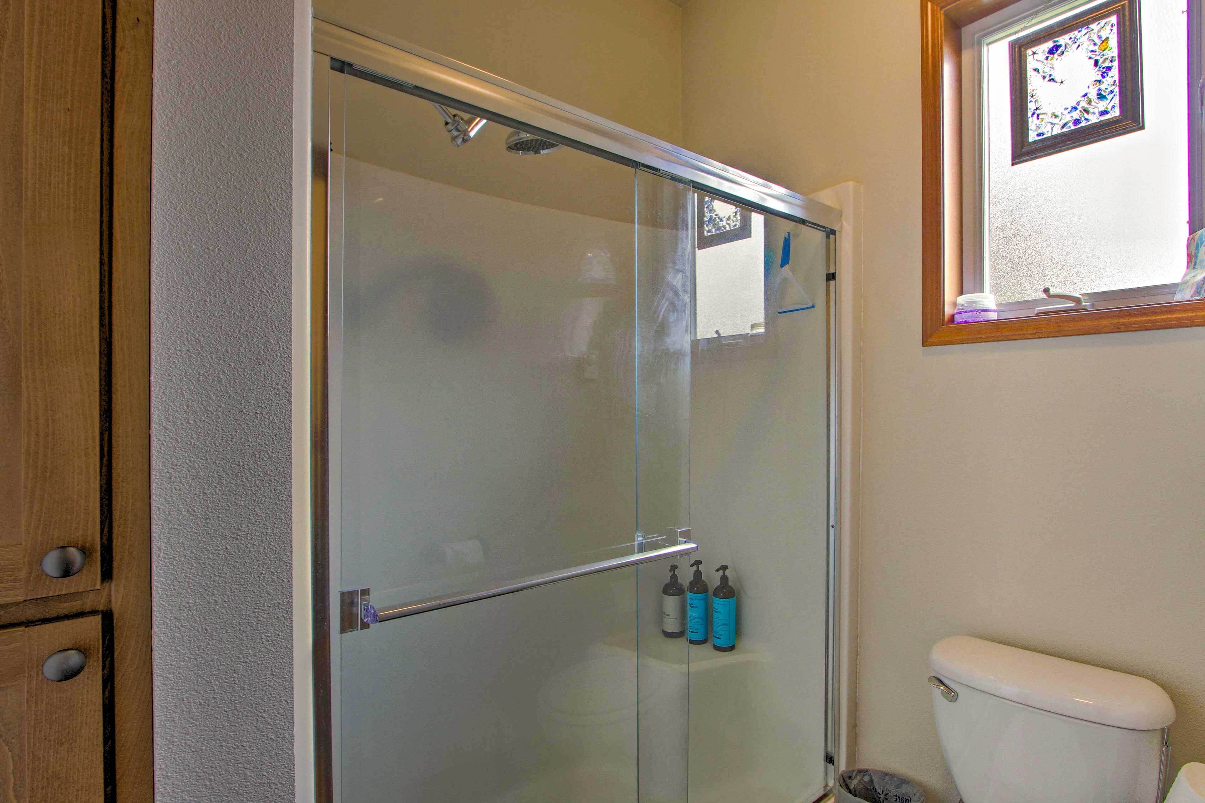 Een badkamer met een douchecabine van glas, een toilet en twee shampoos op de muur.
