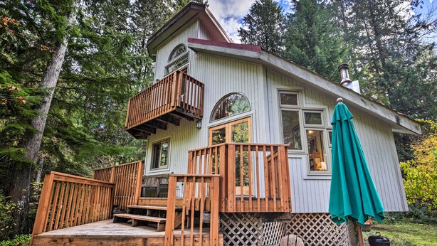 A two-story wooden cabin with a balcony, a deck, and a green umbrella. - River Views, Private Hot Springs Tub, Forest, Deck (Blue River)