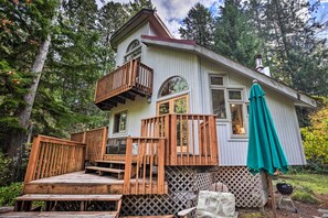 A two-story wooden cabin with a balcony, a deck, and a green umbrella. - River Views, Private Hot Springs Tub, Forest, Deck (Blue River)