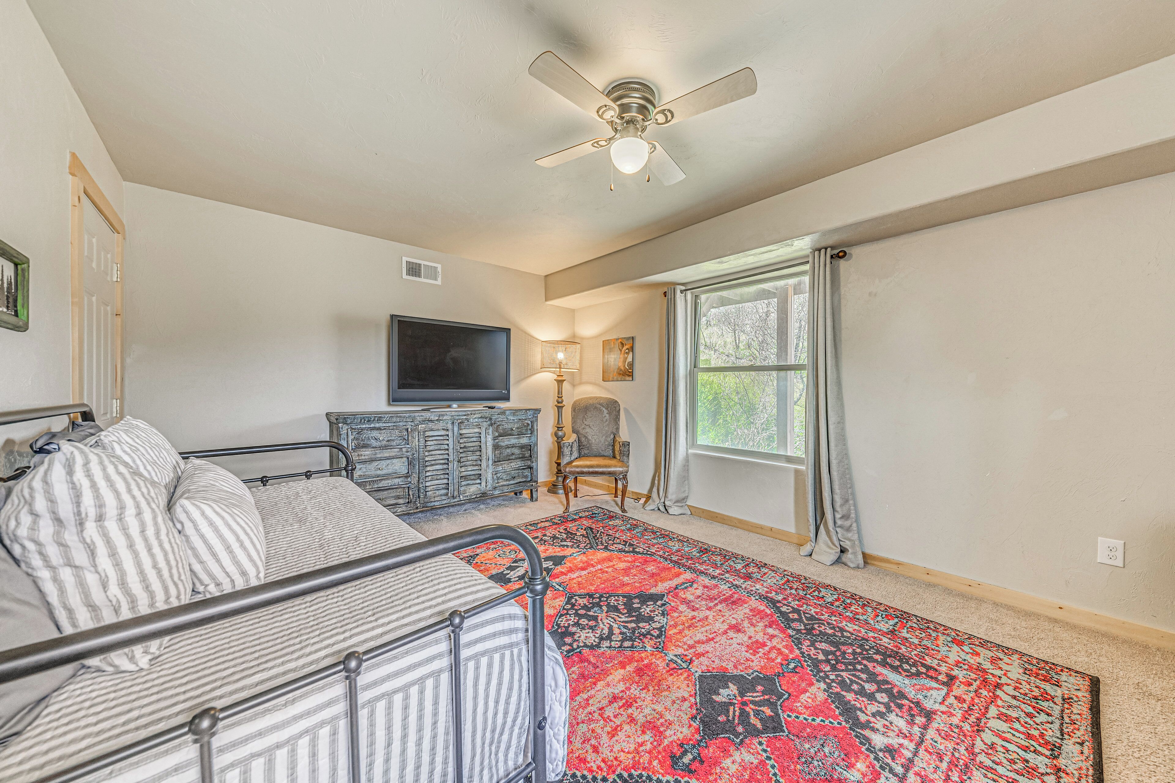A bedroom with a bed, a TV, a chair, a lamp, and a window with curtains.