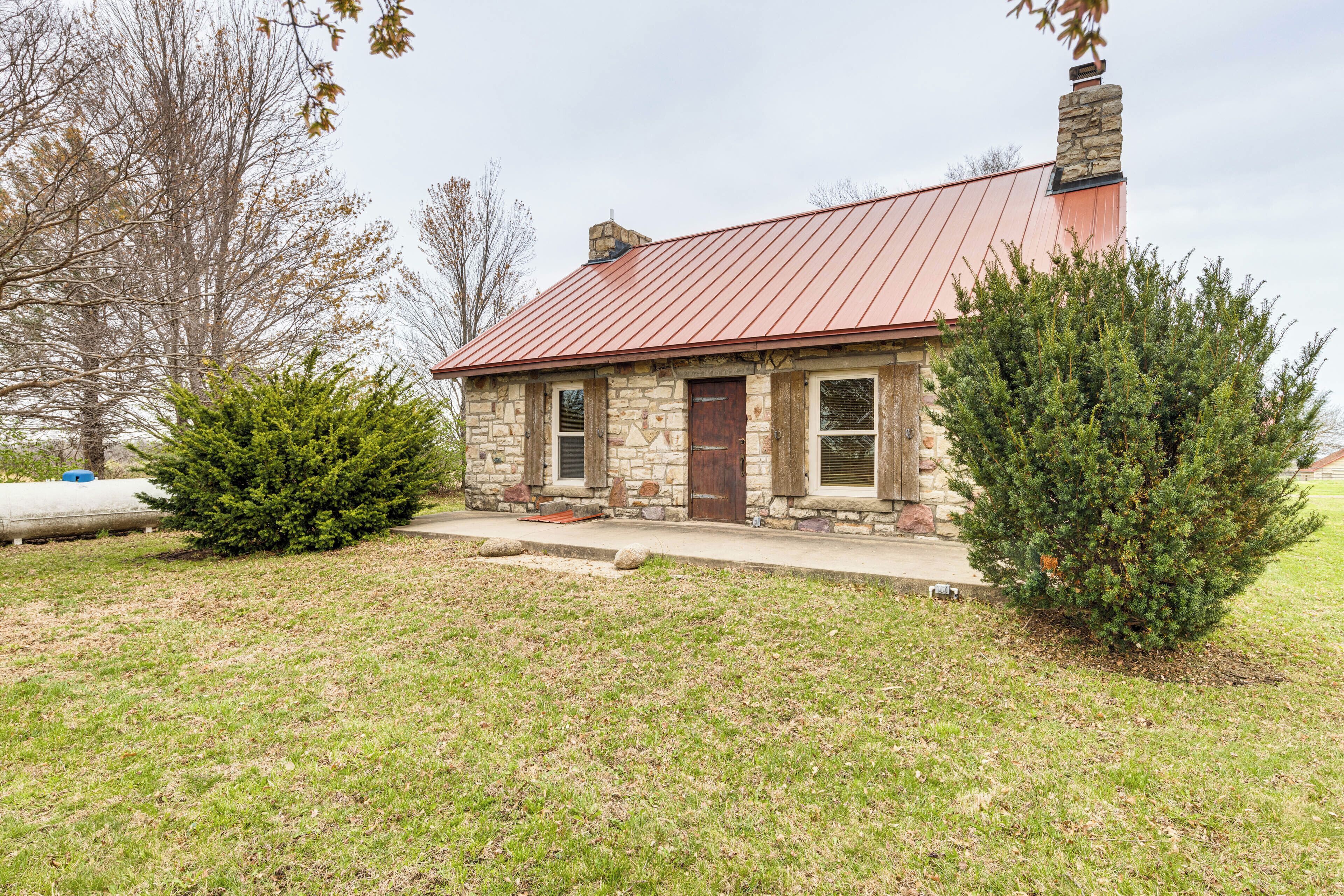 A stone house with a red metal roof, a chimney, and a well-maintained lawn.