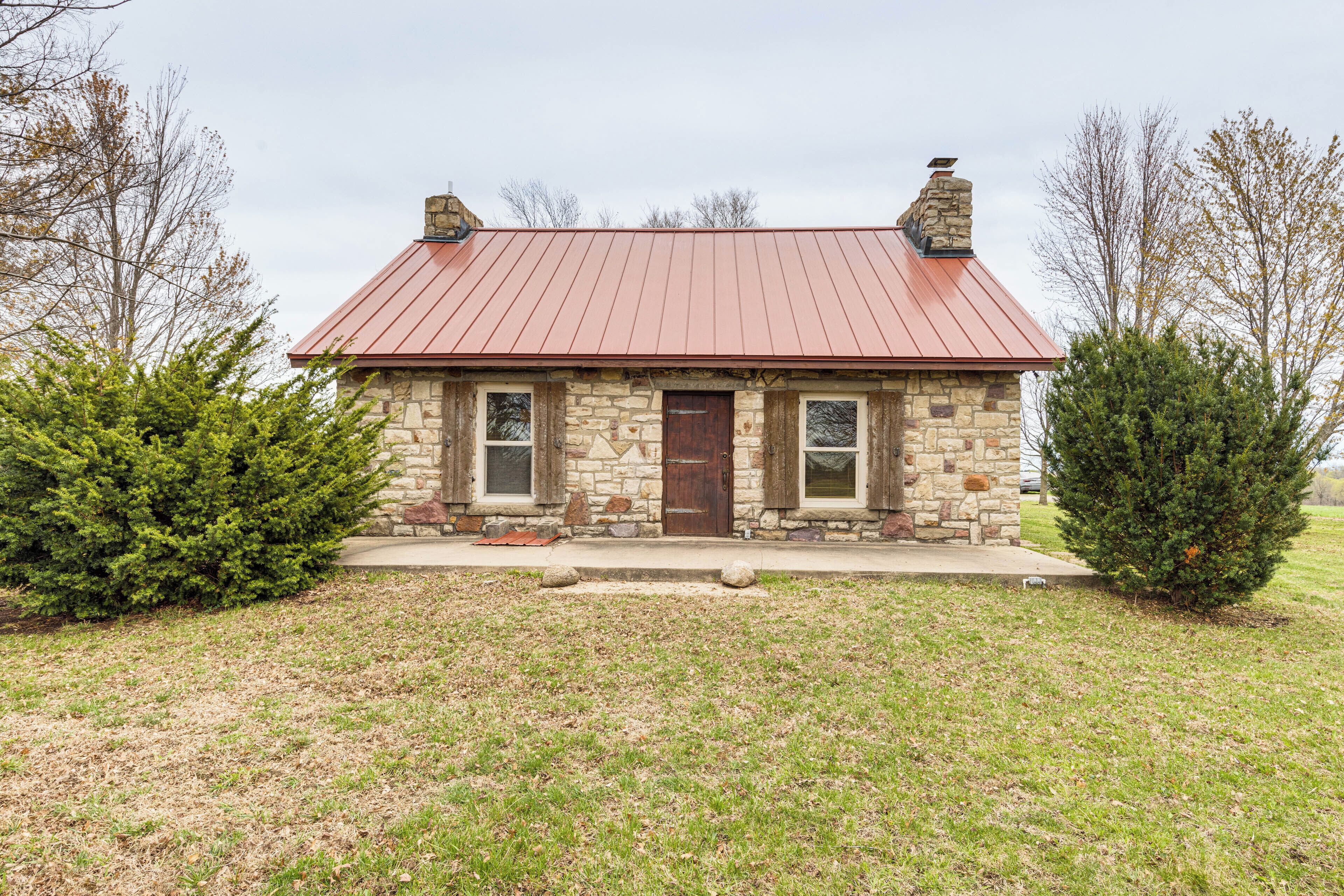 A stone house with a red metal roof, two windows, and a front door.