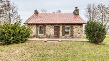 A stone house with a red metal roof, two windows, and a front door.