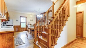 Une cuisine spacieuse, dotée de meubles en bois, et un coin repas avec une table et des chaises. Un escalier en bois, muni d’une rampe, mène à une autre pièce.