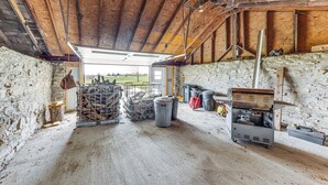 L’intérieur d’une grange rustique, avec des poutres en bois, un plancher en béton et divers éléments de rangement, notamment des bacs et un chariot en métal.