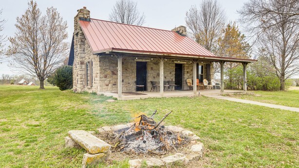 Un bâtiment en pierre avec un toit rouge, un porche et un foyer au premier plan.