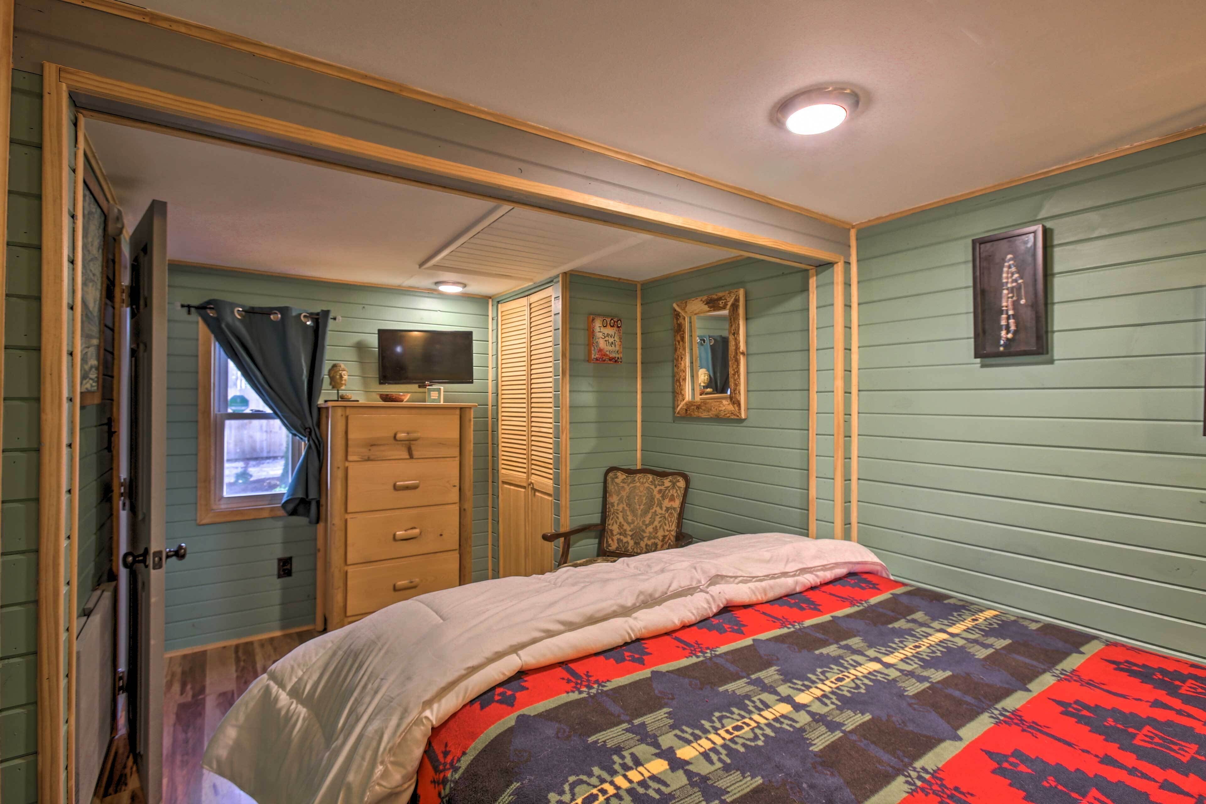 A bedroom with a bed, dresser, chair, and a mirror on the wall.