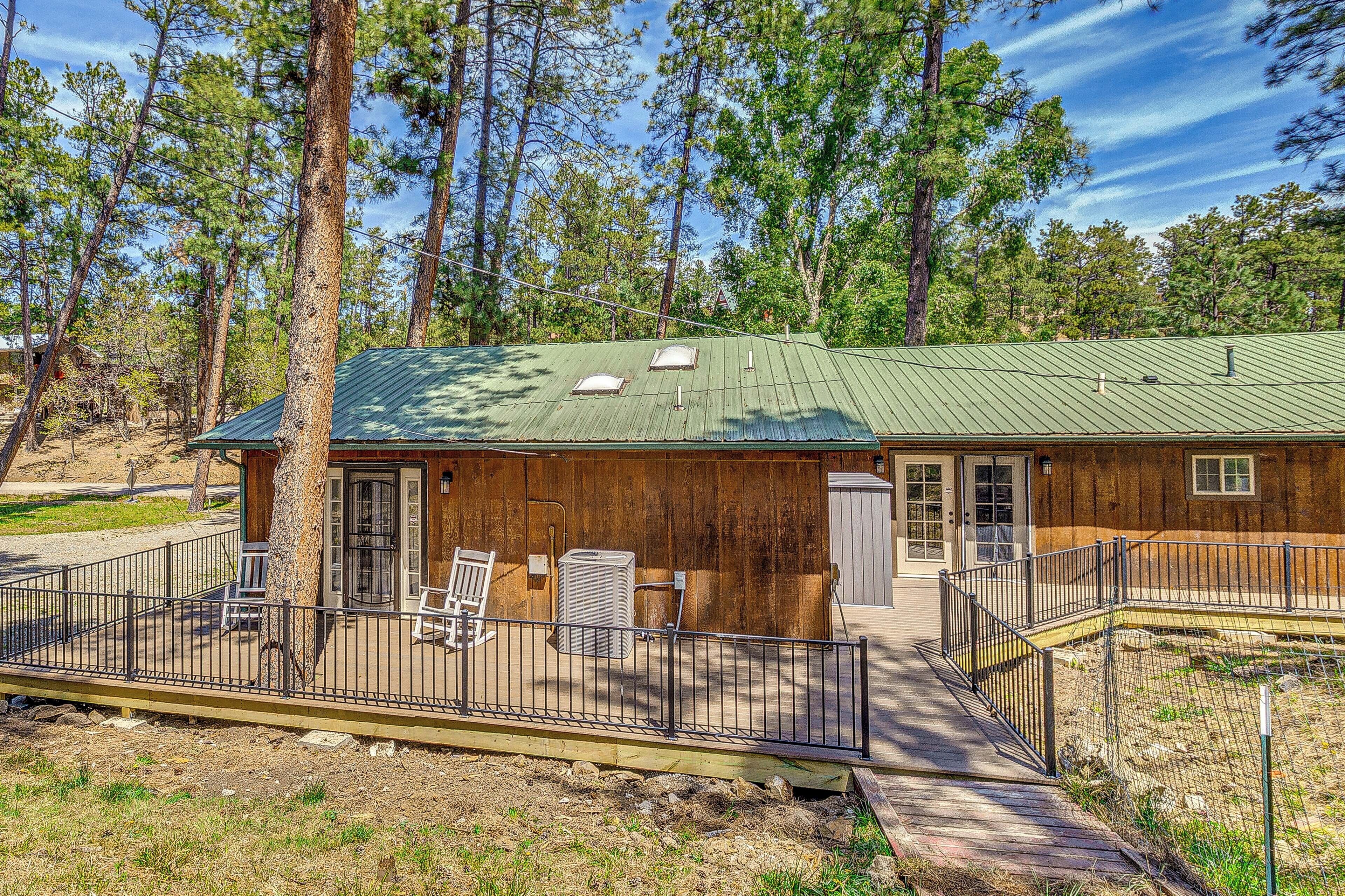 A rustic cabin with a green roof, a fenced deck, and a wooden exterior.