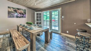 Un comedor con una mesa de madera y bancos, un cuadro de un oso, y vistas al exterior a través de puertas de vidrio.