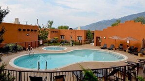 A swimming pool with a sunken center, surrounded by lounge chairs and umbrellas, with a mountain backdrop. - 3 Bedroom Townhome in Osoyoos with views! VII (Osoyoos)