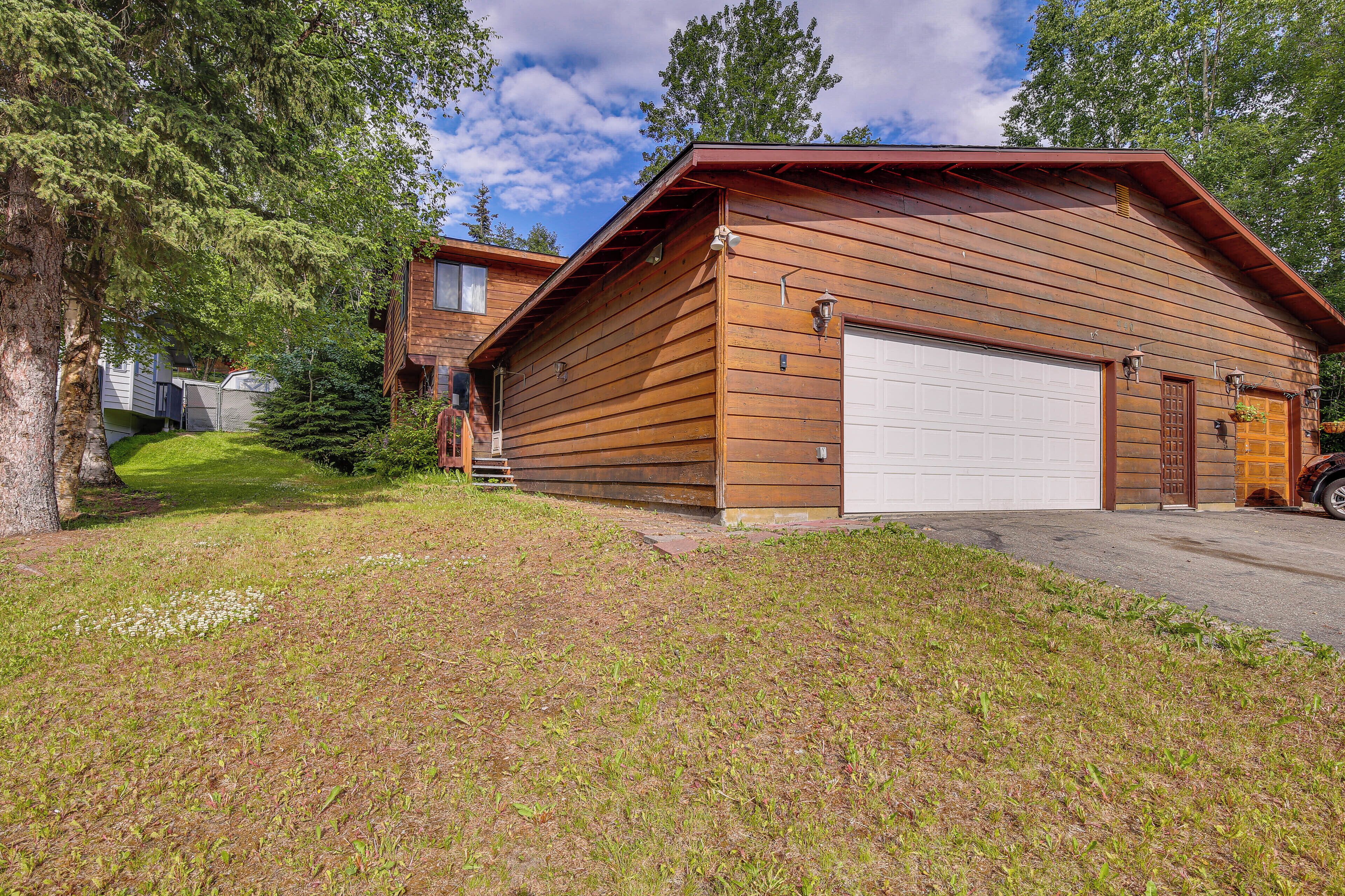 Une cabane en bois avec un garage, entourée d’arbres et bordée d’une pelouse.