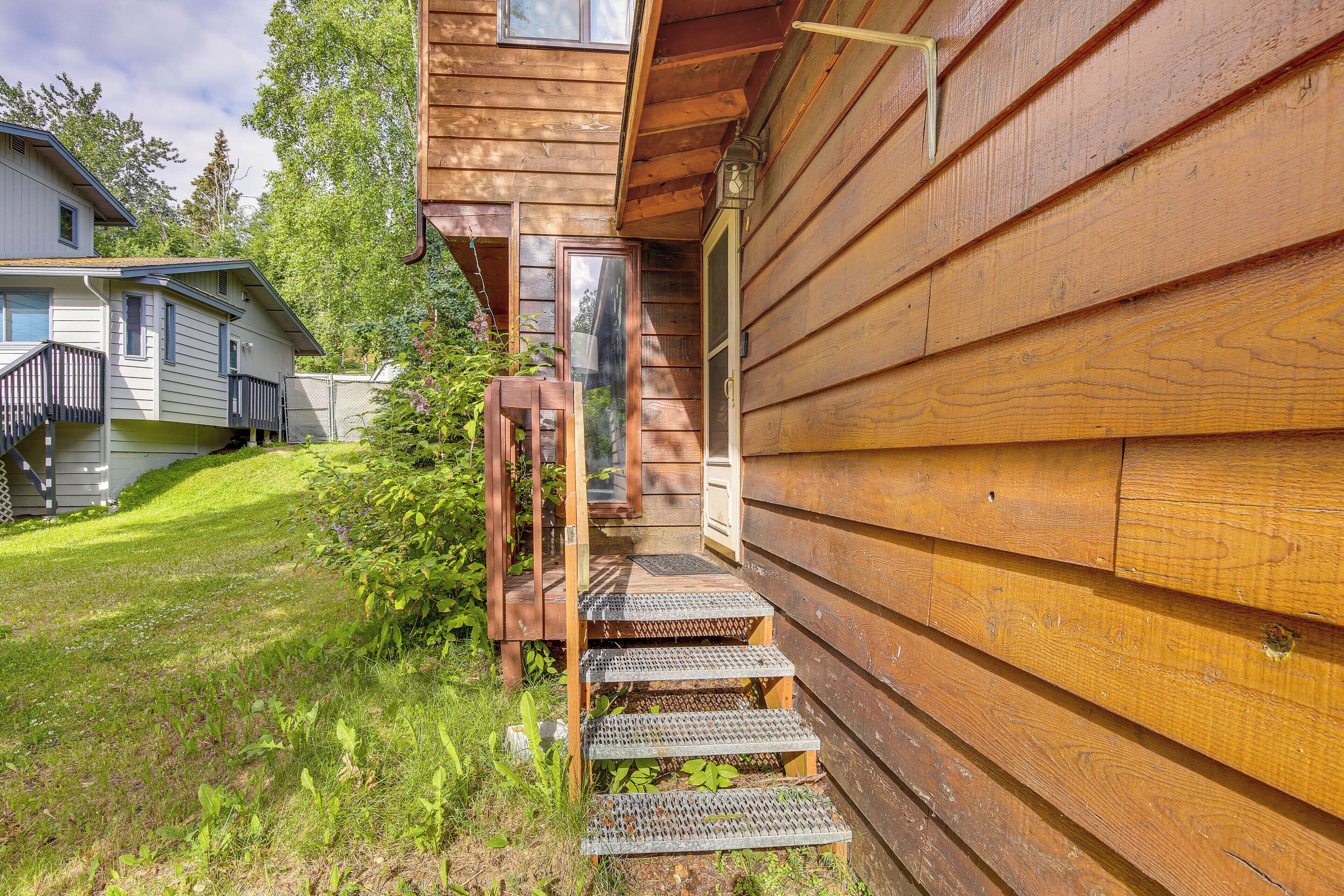 Une cabane en bois avec un escalier en bois menant à une porte, le tout entouré d’une cour verdoyante.