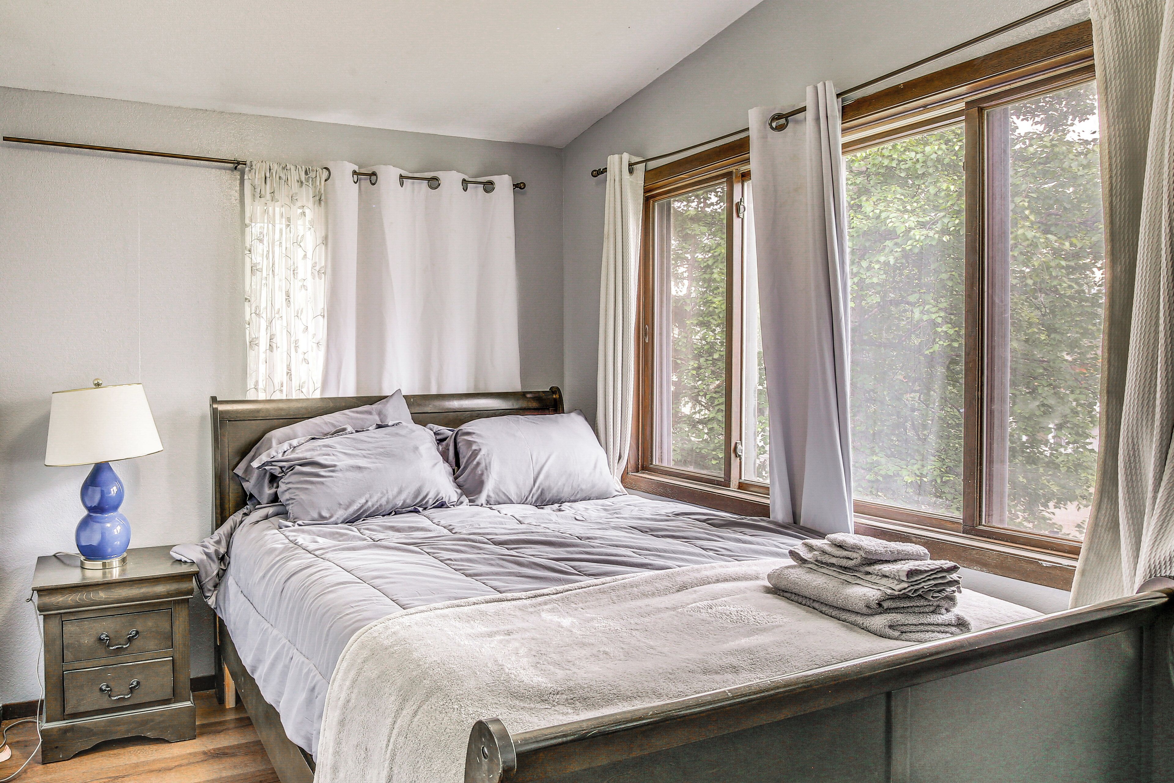 Un dormitorio con cama, mesita de noche, lámpara y ventana con cortinas.