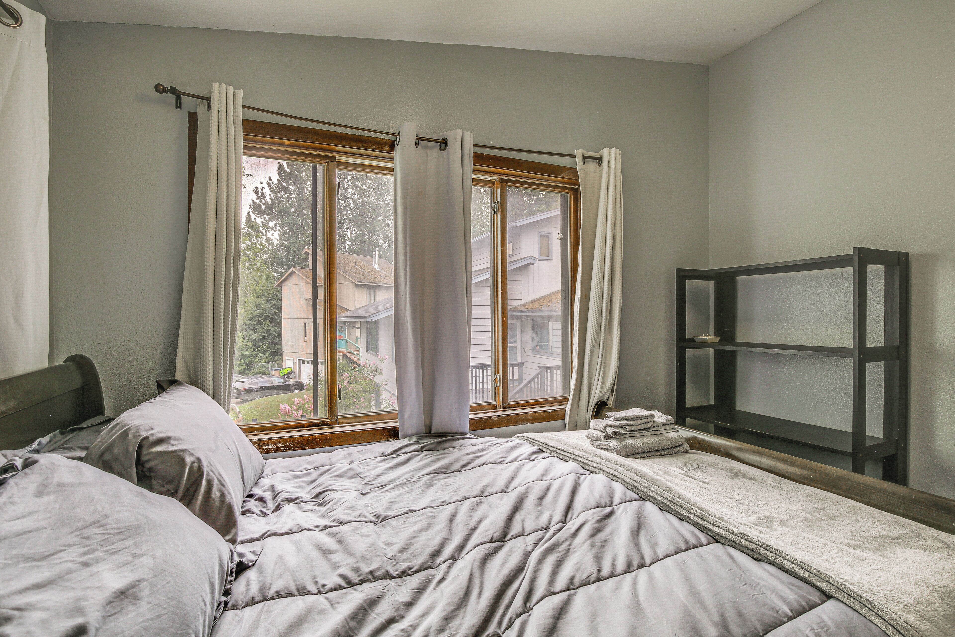 A bedroom with a bed, a window with curtains, and a small shelf.