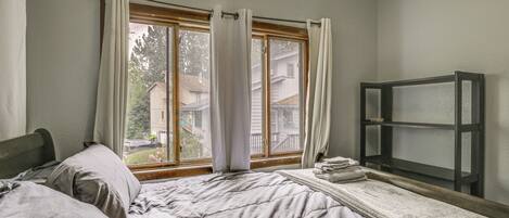 A bedroom with a bed, a window with curtains, and a small shelf.