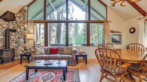 A cozy living room with a stone fireplace, a plaid sofa, a coffee table, and a dining table with chairs.
