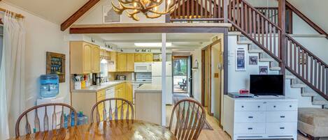 A spacious dining area with a wooden table and chairs, a kitchen with yellow cabinets, and a staircase leading to an upper level.