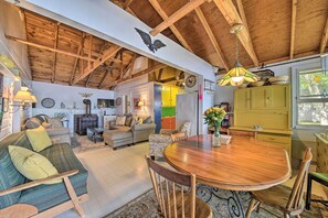A cozy living room with a wooden ceiling, a dining table with chairs, a sofa, and a kitchen area with cabinets and a window. - Quiet & Lovely Lakefront Cottage for Families! (Union)