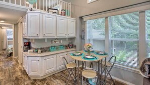 A kitchen with white cabinets, a dining table with teal placemats, and a window with blinds. - Cozy Broken Bow Getaway w/ Fire Pit, 5 Mi to Lake! (Broken Bow)