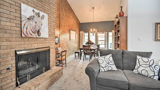 A living room with a fireplace, a gray sofa, and a dining area with a chandelier. - Lubbock Townhome w/ Grill Near TTU & Downtown! (Lubbock)