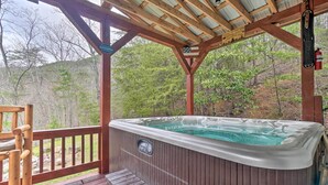 A hot tub on a wooden deck with a pergola overhead, surrounded by trees.