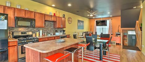 A modern kitchen with wooden cabinets, a central island with bar stools, a microwave, and a stove.