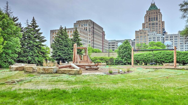 A park with a playground, trees, and a large building in the background. - Urban Escape w/ Patio - 2 Mi to Downtown Detroit! (Detroit)