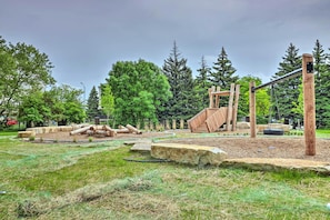 A playground with wooden structures, including a slide and climbing frames, surrounded by trees and grassy areas. - Urban Escape w/ Patio - 2 Mi to Downtown Detroit! (Detroit)