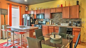 A modern kitchen with wooden cabinets, a stainless steel refrigerator, a microwave, and a large island with bar stools. - Urban Escape w/ Patio - 2 Mi to Downtown Detroit! (Detroit)