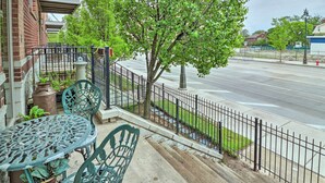 A balcony with a metal table and chairs, a potted plant, and a view of a street with a fence and trees. - Urban Escape w/ Patio - 2 Mi to Downtown Detroit! (Detroit)