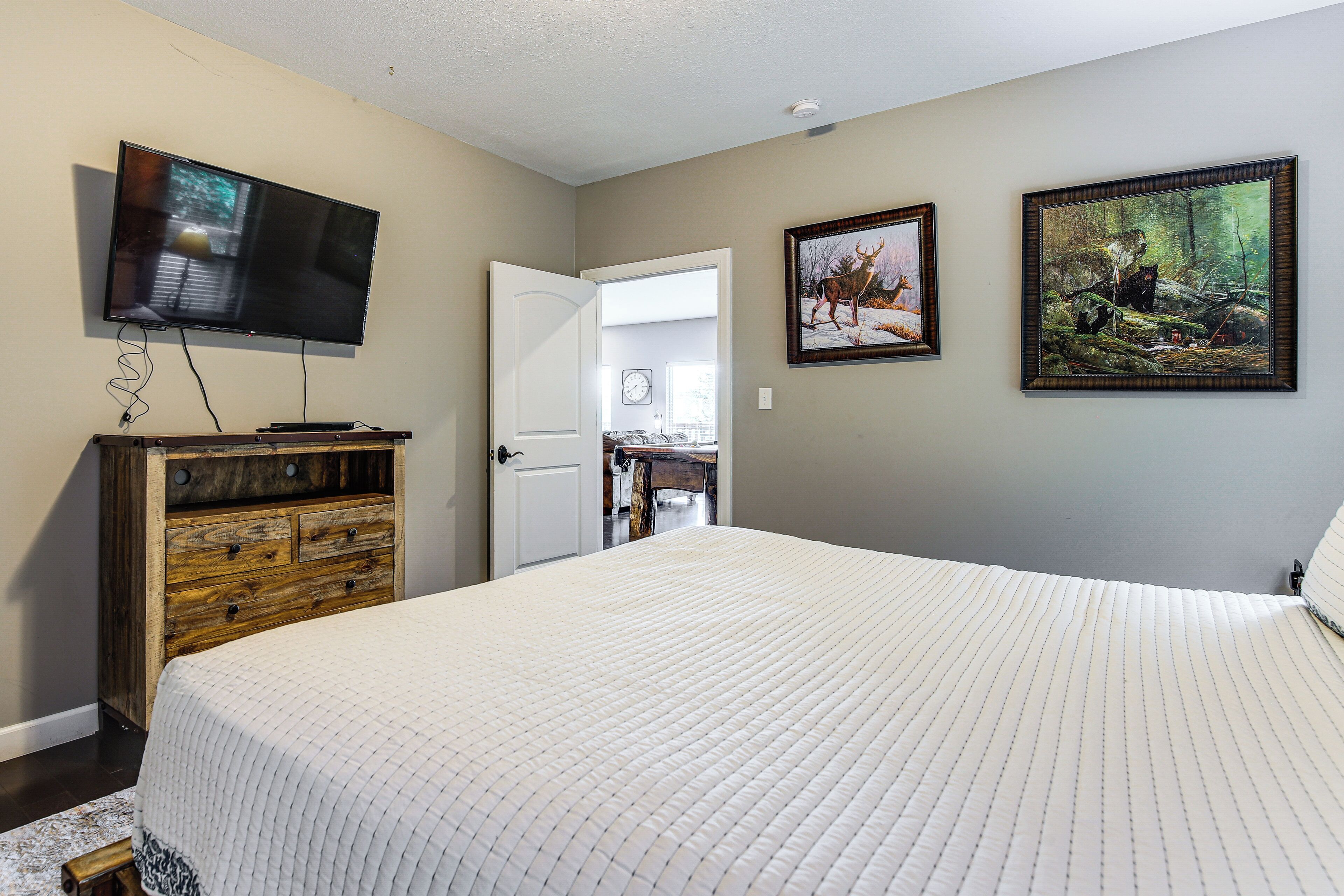 A bedroom with a bed, a television, a wooden dresser, and two framed pictures on the wall.