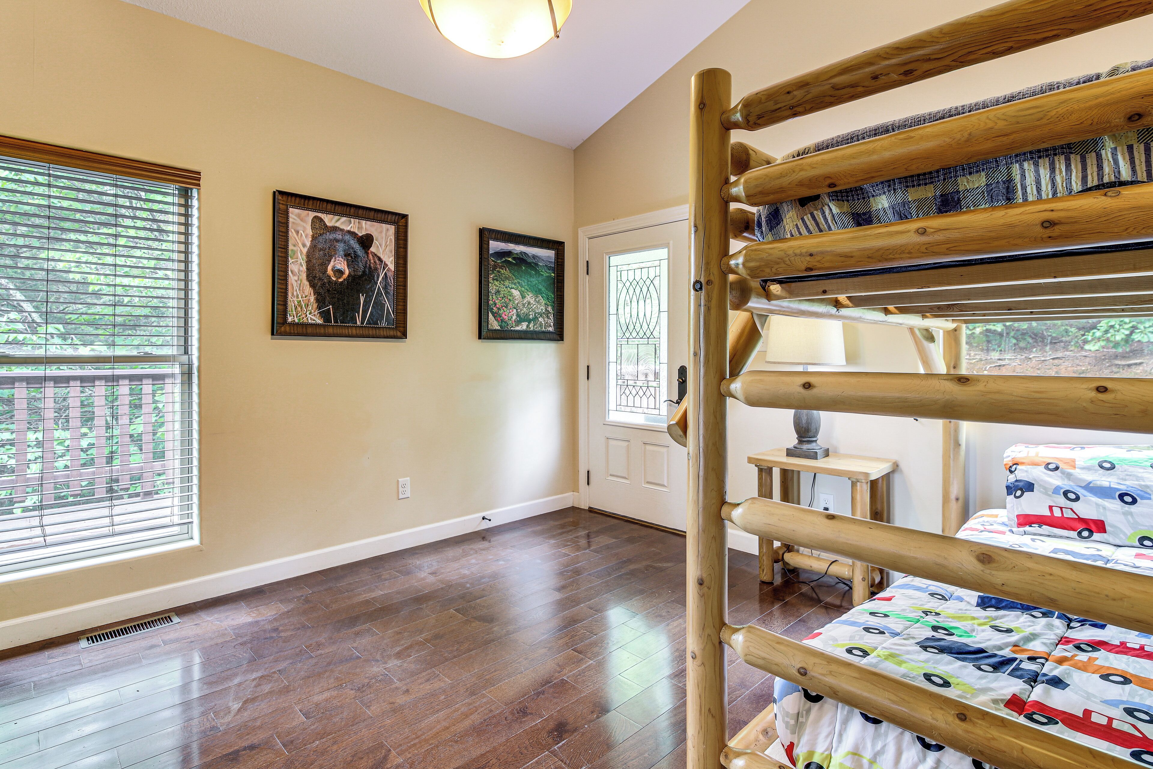 Une chambre avec un lit superposé, un plancher en bois, une fenêtre avec des stores et deux tableaux encadrés au mur.
