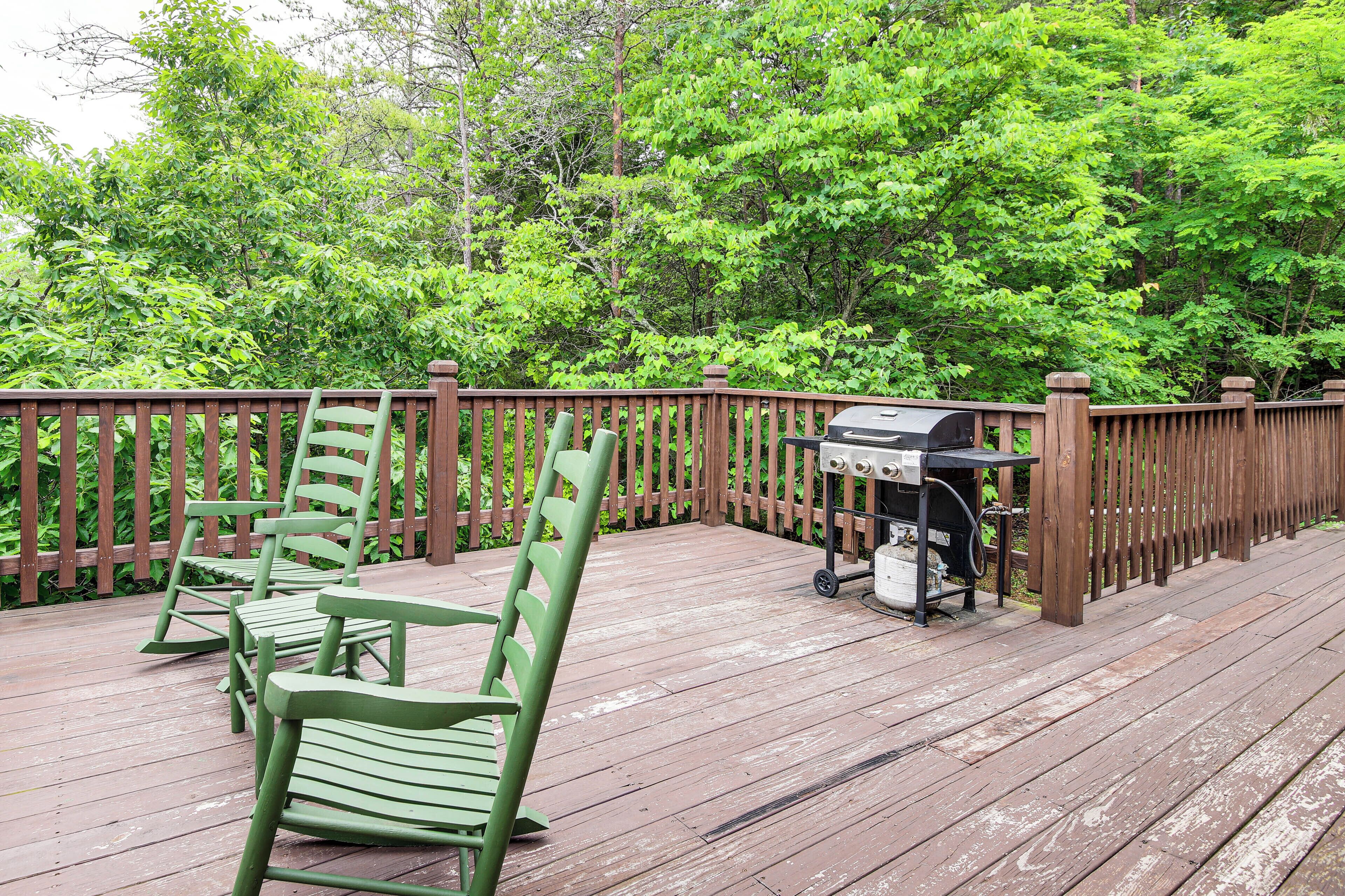 A wooden deck with a grill and green chairs.