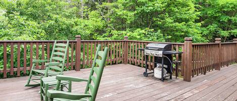 A wooden deck with a grill and green chairs.