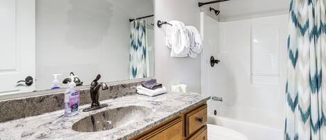 A bathroom with a marble sink, wooden cabinets, a white toilet, a bathtub, and a shower curtain with a blue pattern.