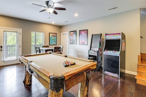 Une table de billard avec un cadre en bois, un ventilateur de plafond et des jeux d’arcade.