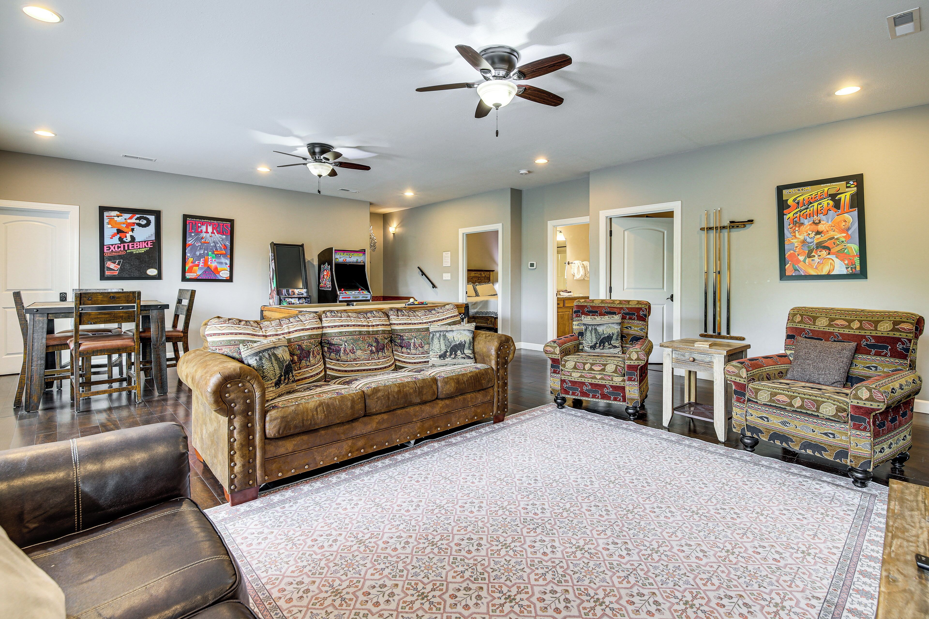 A living room with a brown leather sofa, patterned armchairs, a ceiling fan, and a large rug.