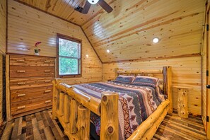 A wooden cabin bedroom with a bed, dresser, and window.