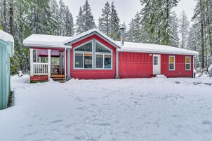 Une cabane rouge avec un porche et une cheminée, entourée d’arbres couverts de neige.