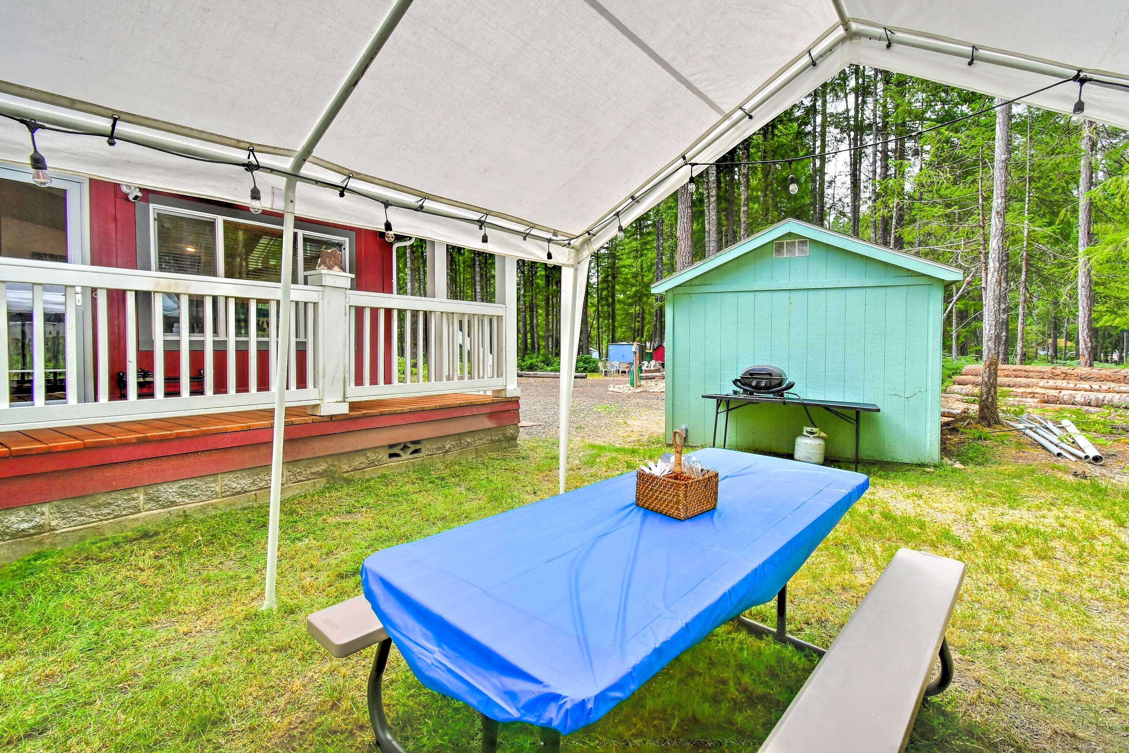 A covered outdoor area with a picnic table and benches, a small shed, and a wooden deck with railings.