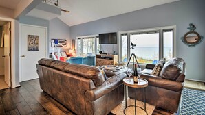 A living room with a brown leather sofa, a small side table with a wine glass, and a television mounted on the wall. - Fire Pit, Smart TV: Waterfront Charlevoix Home (Charlevoix)