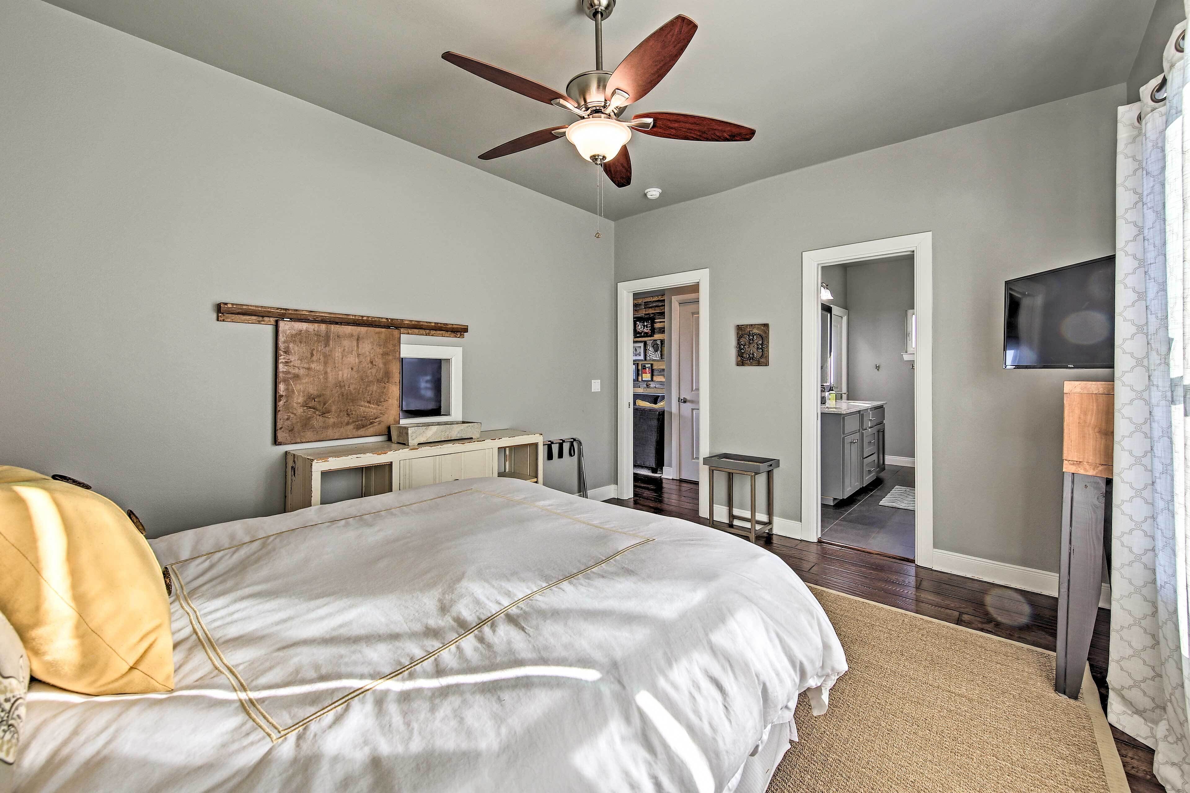 A bedroom with a bed, a ceiling fan, a TV, a desk, and a wardrobe.