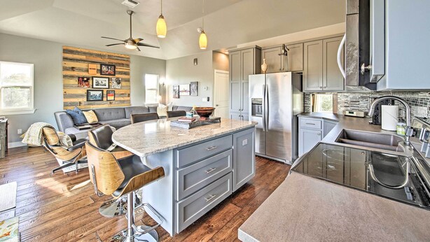 A modern kitchen with a central island, stainless steel appliances, and a dining area with a sofa and chairs. - Peaceful Hill Country Hideaway w/ Pond Views (Wimberley)