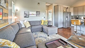 A modern living room with a sectional sofa, a coffee table, and a kitchen area with stainless steel appliances. - Peaceful Hill Country Hideaway w/ Pond Views (Wimberley)