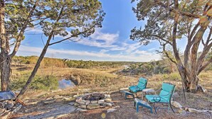 A campsite with a fire pit, two green chairs, and a view of a valley. - Peaceful Hill Country Hideaway w/ Pond Views (Wimberley)